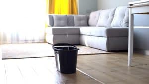 A bucket in a living room catching drops of water coming from a leaking ceiling