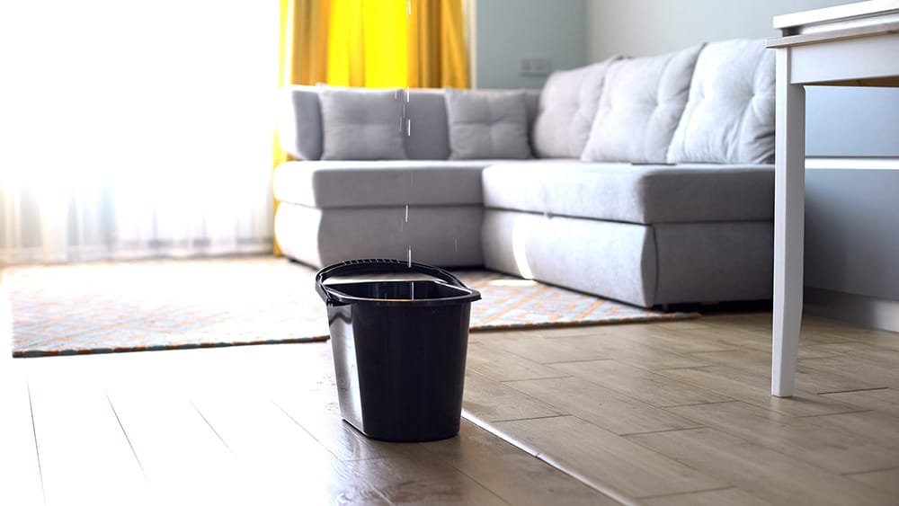 A bucket in a living room catching drops of water coming from a leaking ceiling
