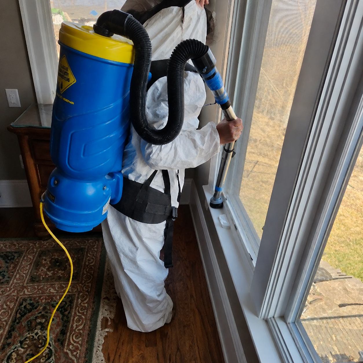 Restoration technician wearing protective equipment with HEPA vacuum equipment during controlled cleaning.