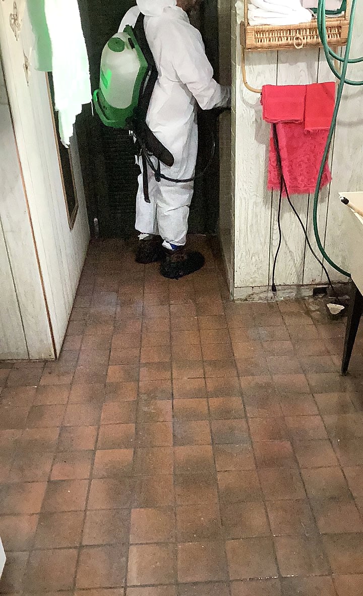Restoration technician in protective clothing cleaning an affected interior work area