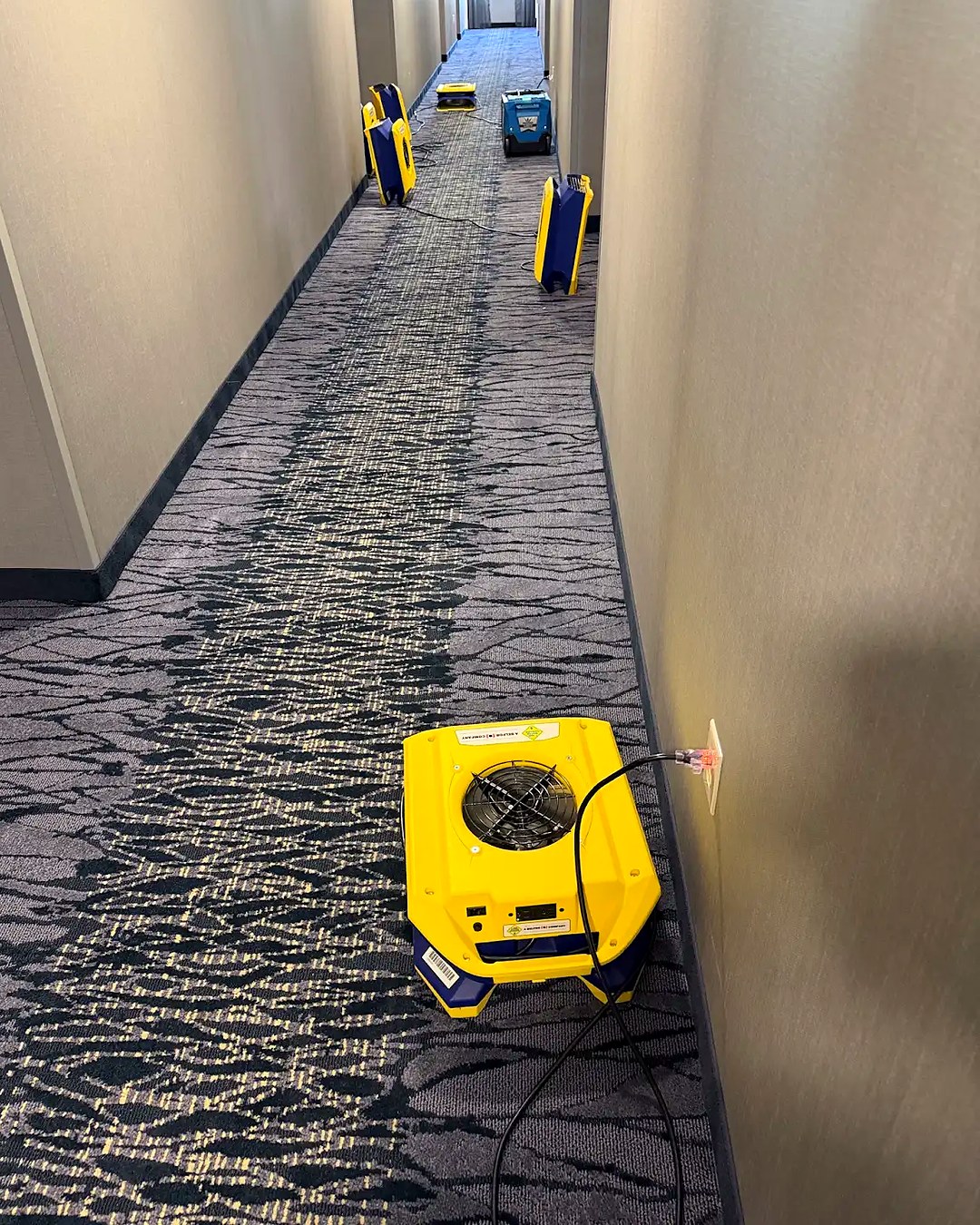 Multiple air movers positioned along a hotel hallway during water damage drying