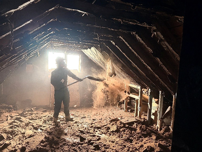 Technician working inside a fire-damaged attic with charred framing and loose debris
