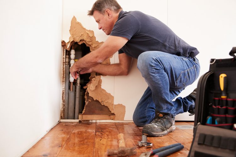 A technician is fixing a burst pipe in a home