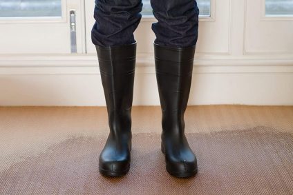 A person wearing rubber boots while standing on a carpet that has standing water
